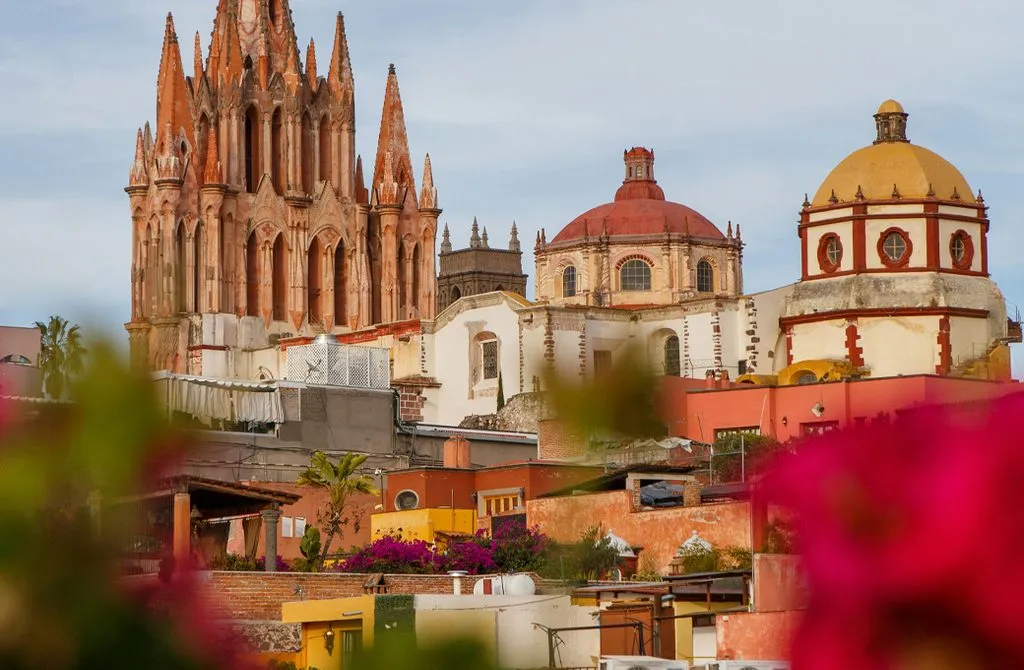 The Parroquia and church domes of San Miguel de Allende rising above the rooftops, framed by pink bougainvillea