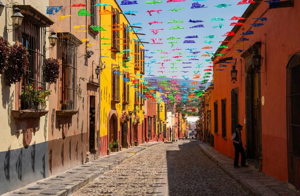 A sunny San Miguel de Allende street decorated with colorful papel picado banners above the cobblestones
