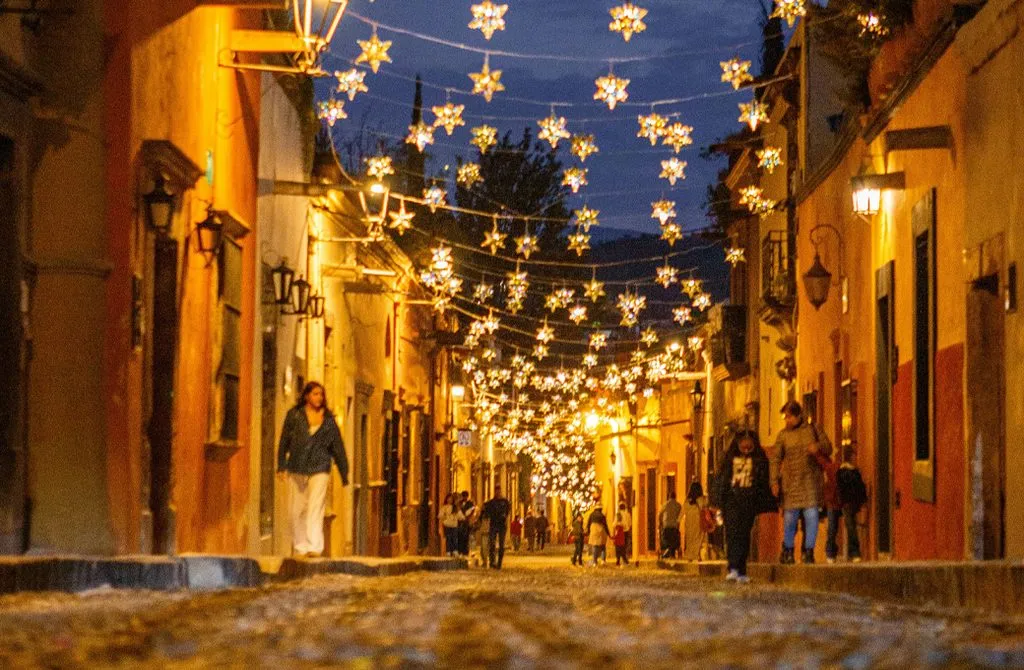 A cobblestone street in San Miguel de Allende at dusk strung with glowing star lanterns overhead