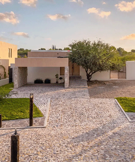 A single-level Mítico residence with a stone driveway and mature tree at golden hour